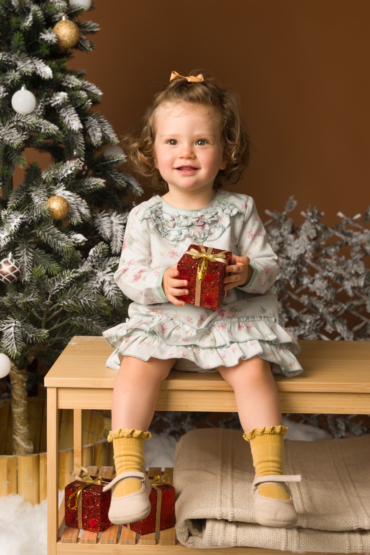 Niña sentada junto a un árbol de Navidad.