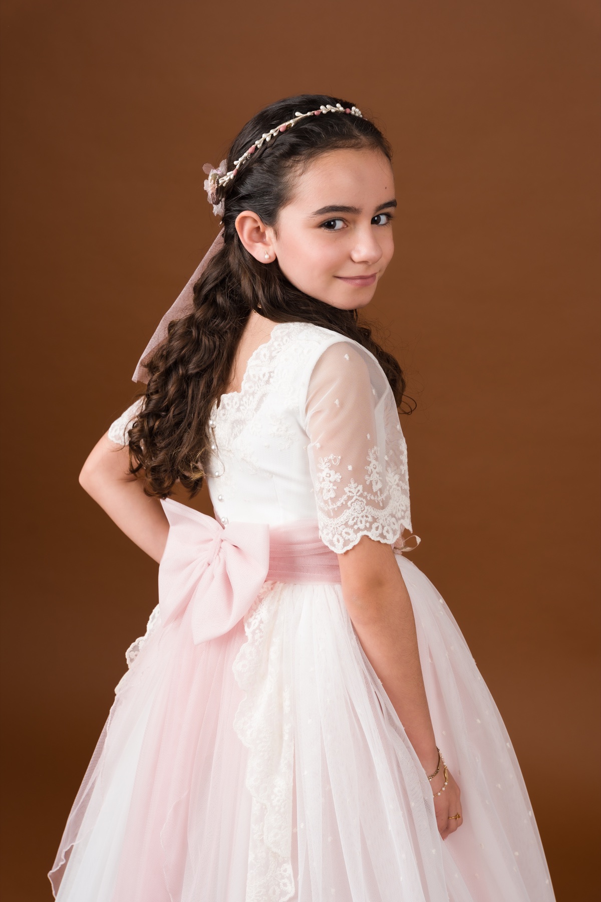 Retrato de una niña con vestido de comunión sobre fondo terracota.
