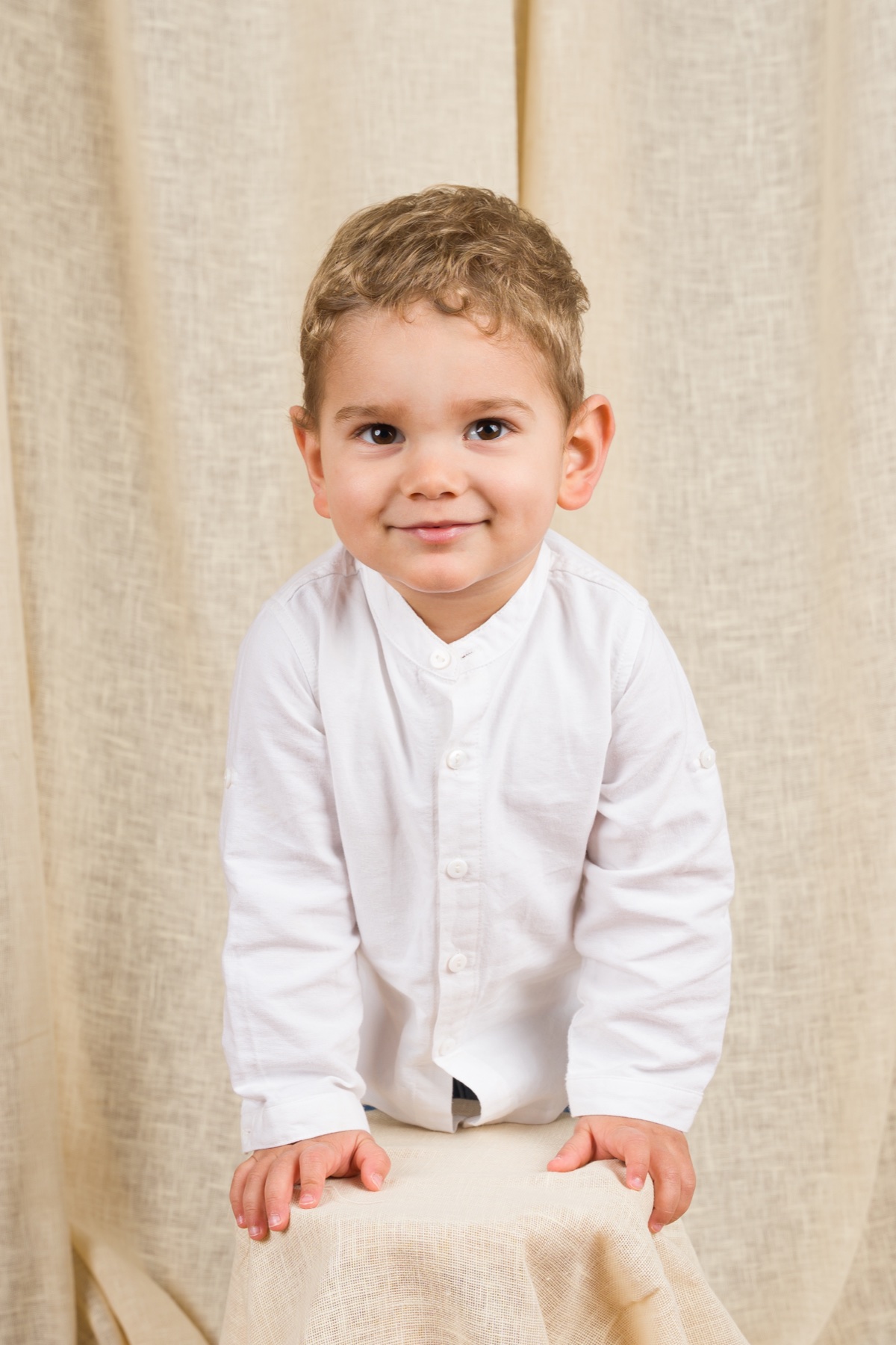 Retrato de un niño con camisa blanca sobre fondo claro.