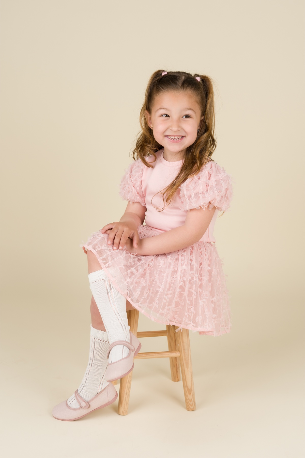 Niña con vestido rosa sentada en un taburete.