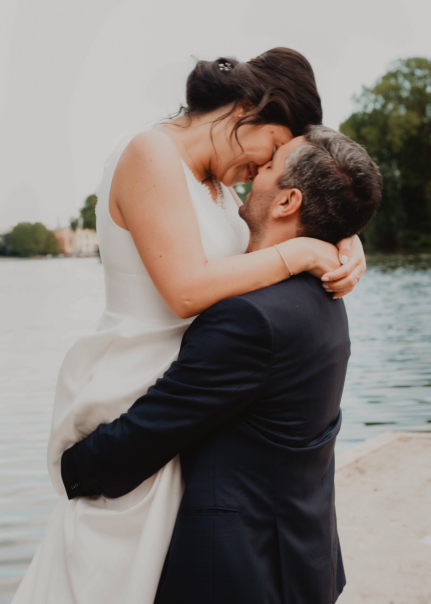 Una pareja de recién casados se abraza junto al agua.