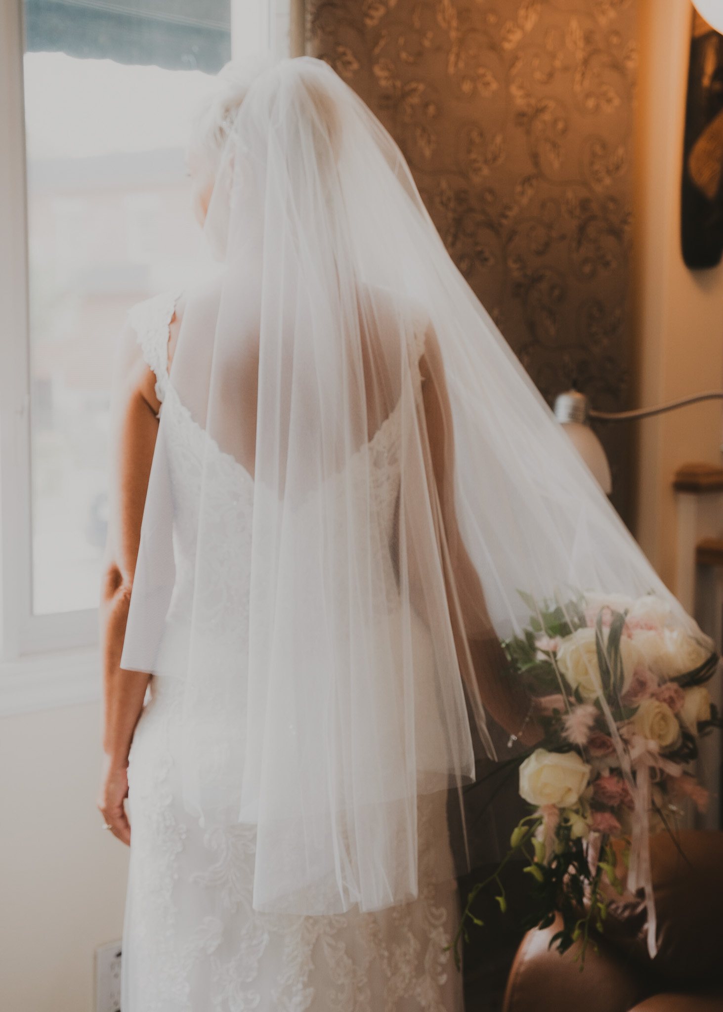 La espalda y el velo de una novia ante la luz de una ventana.