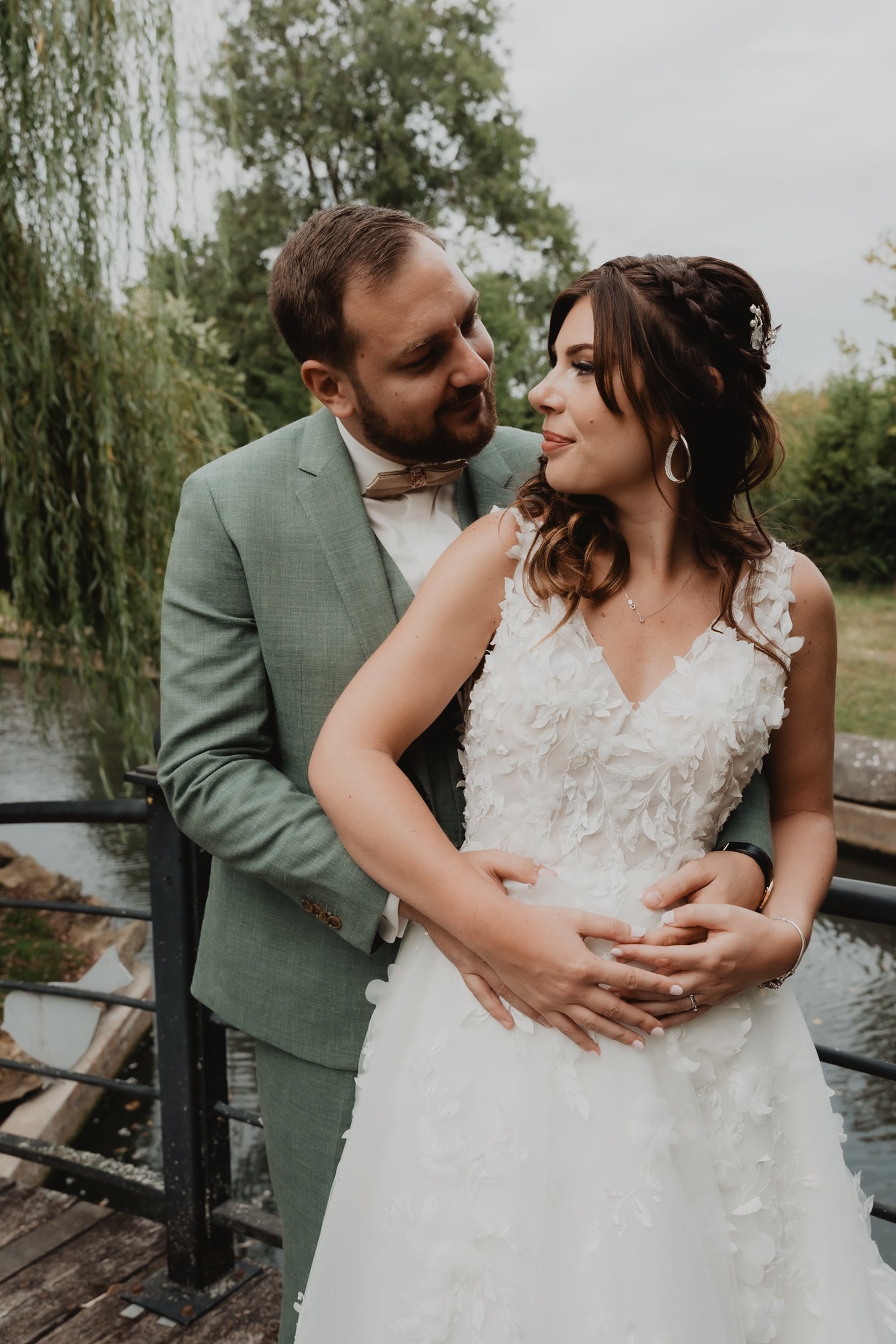 Una pareja con traje verde se abraza entre árboles.