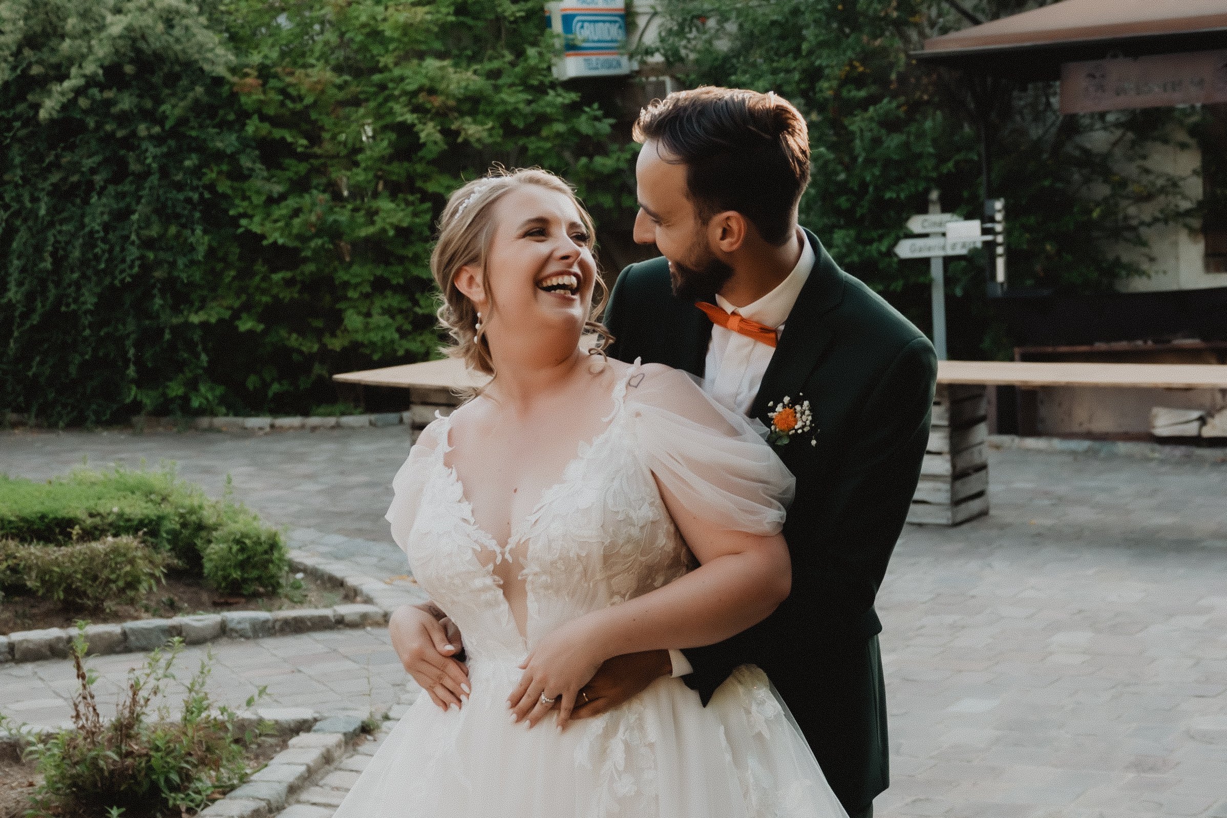 Una pareja de recién casados sonríe mientras camina entre árboles.