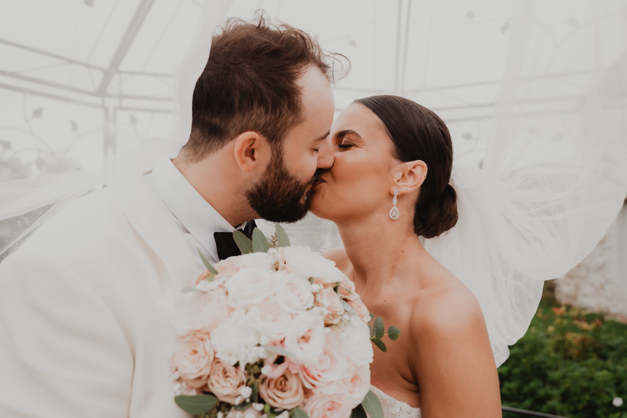 Una pareja se besa tras un ramo de flores claras.